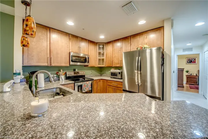 Kitchen with light stone counters, glass insert cabinets, stainless steel appliances, recessed lighting, and brown cabinets