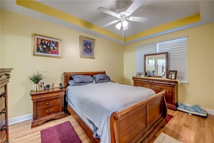 Bedroom featuring a raised ceiling, light wood-style floors, and a ceiling fan