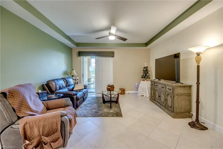 Living area featuring a tray ceiling, light tile patterned floors, and a ceiling fan