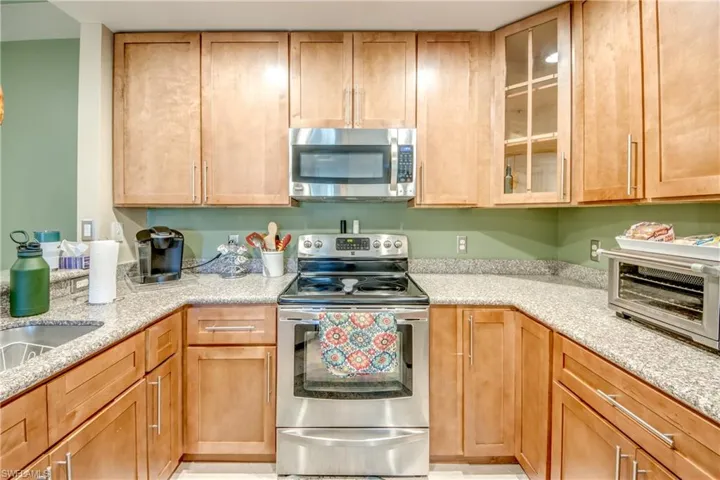 Kitchen with stainless steel appliances, glass insert cabinets, and light stone countertops