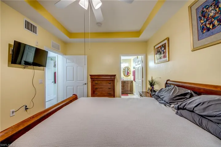 Bedroom with a tray ceiling, ensuite bathroom, and a ceiling fan