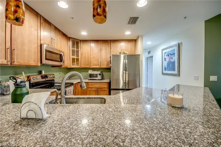 Kitchen featuring glass insert cabinets, light stone countertops, stainless steel appliances, recessed lighting, and brown cabinets