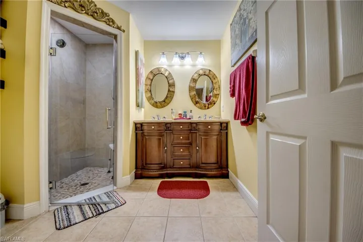 Bathroom with double vanity, light tile patterned floors, and a stall shower