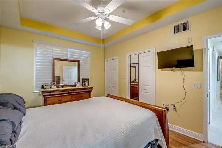 Bedroom featuring a tray ceiling, ensuite bathroom, a ceiling fan, and wood finished floors