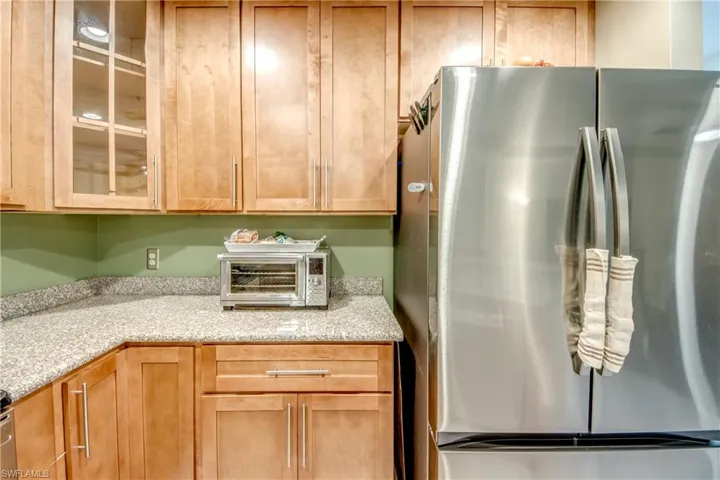 Kitchen featuring freestanding refrigerator, glass insert cabinets, and light stone counters