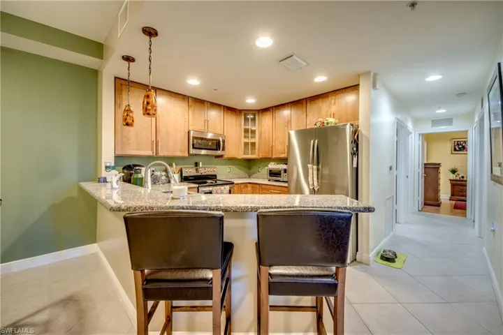 Kitchen featuring a kitchen bar, light stone countertops, stainless steel appliances, a peninsula, and glass insert cabinets