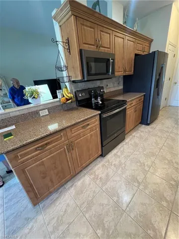 Kitchen featuring wood cabinetry, integrated appliances, granite-style countertops, tiled flooring, and a tiled backsplash