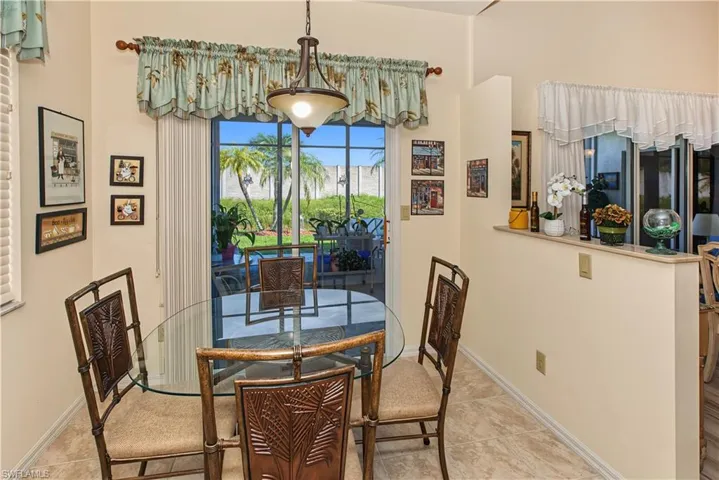 Bright dining area featuring a glass-top table with decorative base, woven-seat chairs with carved wood frames, and expansive glass doors framed by a decorative valance