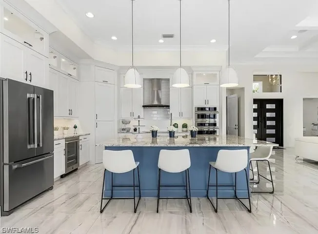 Kitchen featuring stainless steel appliances, a spacious island, white cabinetry, light stone countertops, and glass insert cabinets