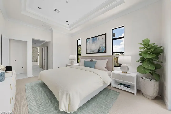 Bedroom with crown molding, light colored carpet, a tray ceiling, and ensuite bath