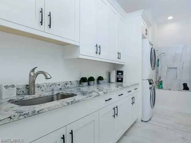 Washroom with estacked washer and dryer, light marble finish floors, and recessed lighting