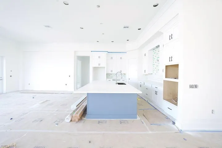 Kitchen with white cabinets, an island with sink, a breakfast bar area, crown molding, and light stone counters