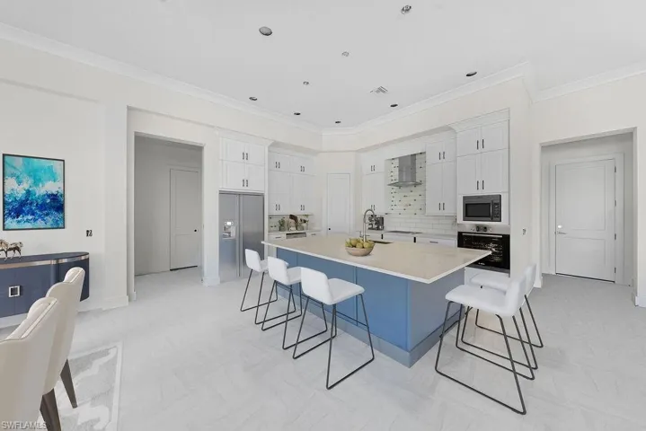Kitchen featuring white cabinets, a kitchen breakfast bar, appliances with stainless steel finishes, a spacious island, and crown molding