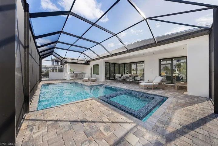 View of swimming pool featuring a sunroom, glass enclosure, a pool with connected hot tub, and a patio area