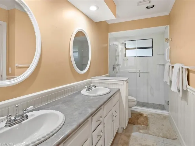 Primary bathroom with updated walk-in shower, double vanity, tiled floors and a wainscoted wall.
