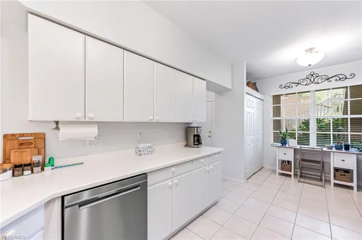 Kitchen with stainless steel dishwasher, white cabinetry, light tile patterned floors, and light countertops