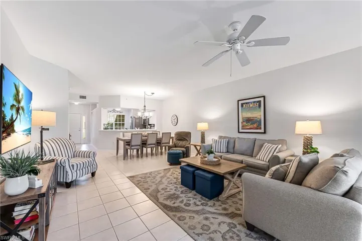 Living area featuring light tile patterned flooring, visible vents, and ceiling fan with notable chandelier