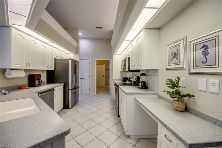 Kitchen featuring backsplash, light tile floors, sink, white cabinets, and appliances with stainless steel finishes