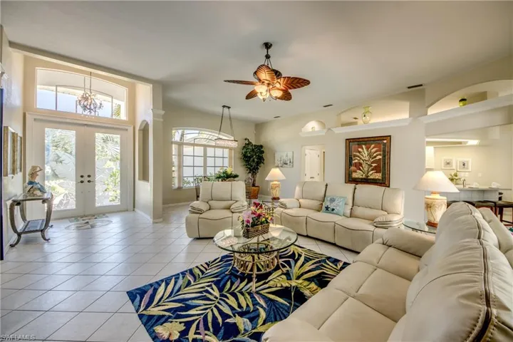 Tiled living room featuring french doors and ceiling fan with notable chandelier