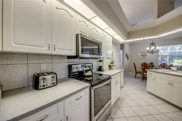 Kitchen with a chandelier, light tile flooring, tasteful backsplash, white cabinetry, and appliances with stainless steel finishes