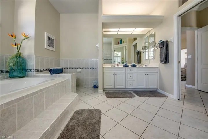 Bathroom featuring dual bowl vanity, tile flooring, and tiled tub