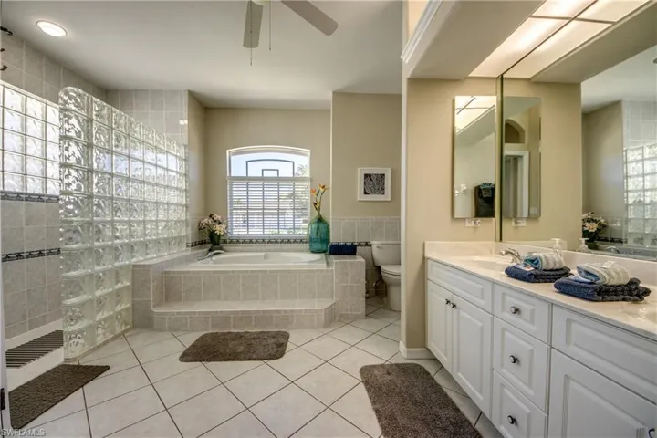 Bathroom with tile floors, a relaxing tiled bath, toilet, and large vanity