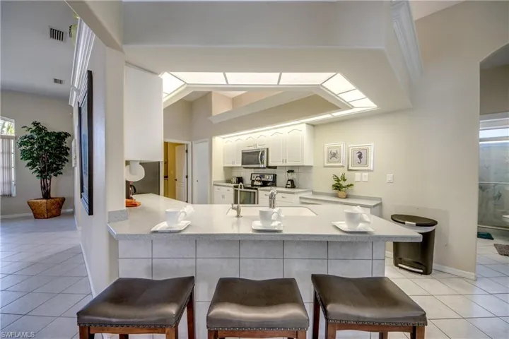 Kitchen featuring appliances with stainless steel finishes, white cabinets, kitchen peninsula, a breakfast bar, and light tile flooring