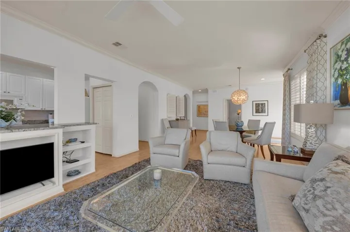 GreaT Room with ornamental molding, arched walkways, light laminate flooring, a ceiling fan, and suspended lighting