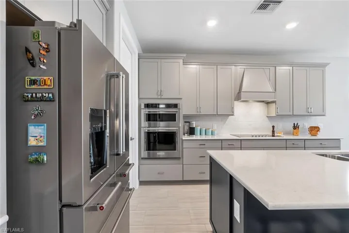 Kitchen with stainless steel appliances, custom exhaust hood, gray cabinetry, tasteful backsplash, and recessed lighting