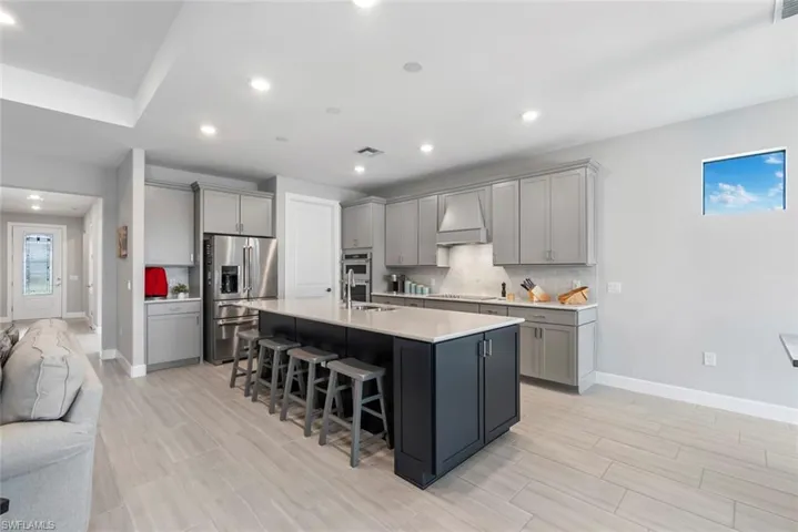 Kitchen with gray cabinetry, stainless steel fridge, tasteful backsplash, a kitchen bar, and recessed lighting