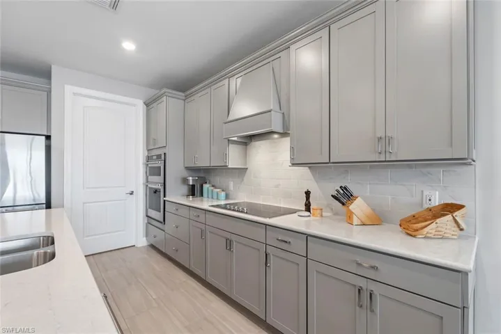 Kitchen featuring gray cabinetry, black electric cooktop, custom range hood, backsplash, and recessed lighting