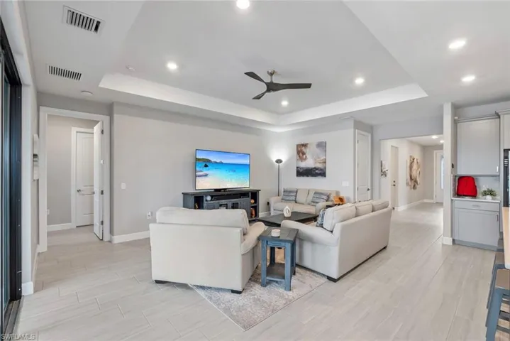 Living area with a raised ceiling, ceiling fan, wood finish floors, and recessed lighting