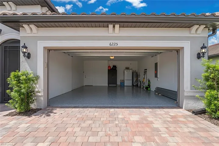 Garage with white fridge, decorative driveway, and electric panel