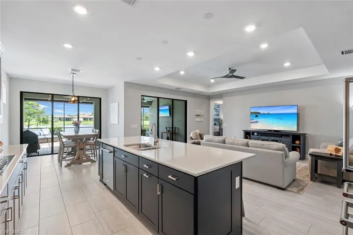 Kitchen featuring light countertops, a raised ceiling, a ceiling fan, an island with sink, and recessed lighting
