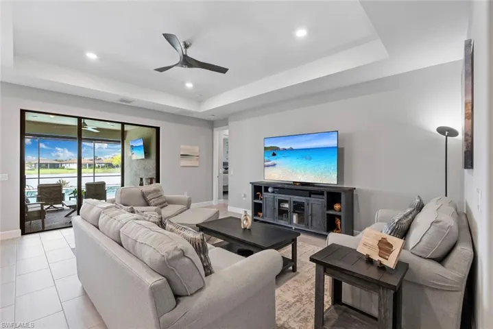 Living area with a tray ceiling, a ceiling fan, recessed lighting, and light tile patterned floors