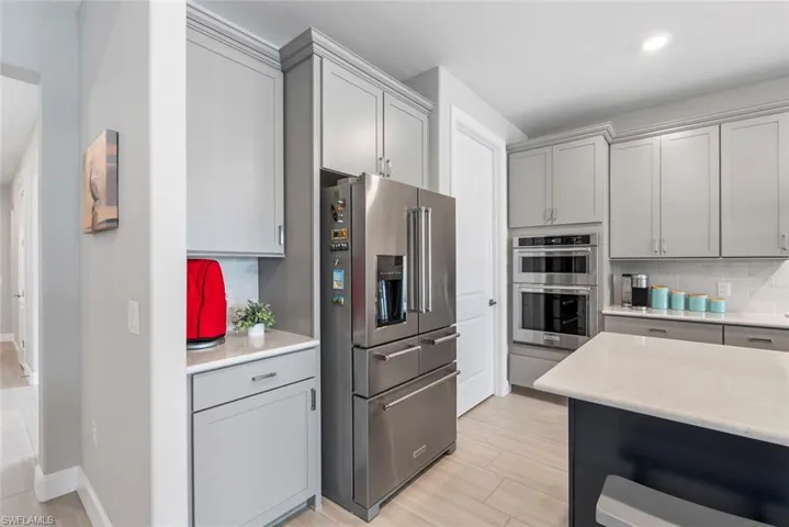 Kitchen with appliances with stainless steel finishes, gray cabinetry, tasteful backsplash, light stone countertops, and recessed lighting