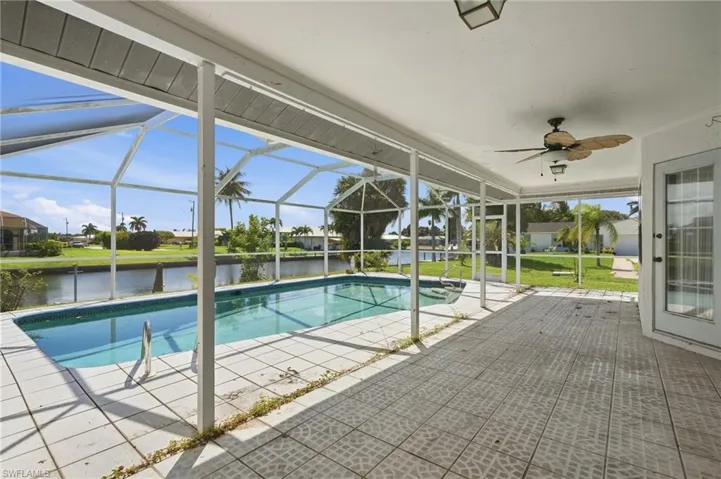 Screened-in pool enclosure featuring a rectangular pool with integrated steps, a ceiling fan, and tiled flooring