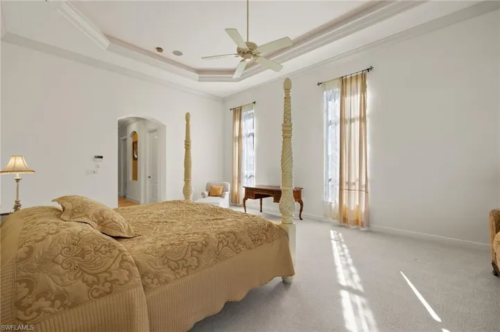 Bedroom featuring a tray ceiling, arched walkways, crown molding, light colored carpet, and baseboards