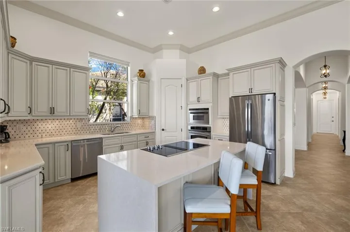 Kitchen with arched walkways, stainless steel appliances, backsplash, a kitchen island, and a sink