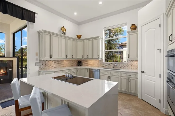 Kitchen with dishwasher, a kitchen island, a kitchen breakfast bar, a lit fireplace, and a sink