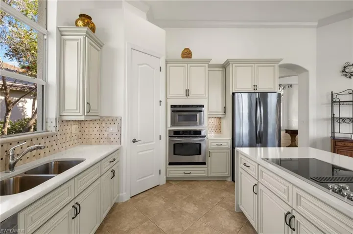 Kitchen with arched walkways, stainless steel appliances, tasteful backsplash, light countertops, and a sink