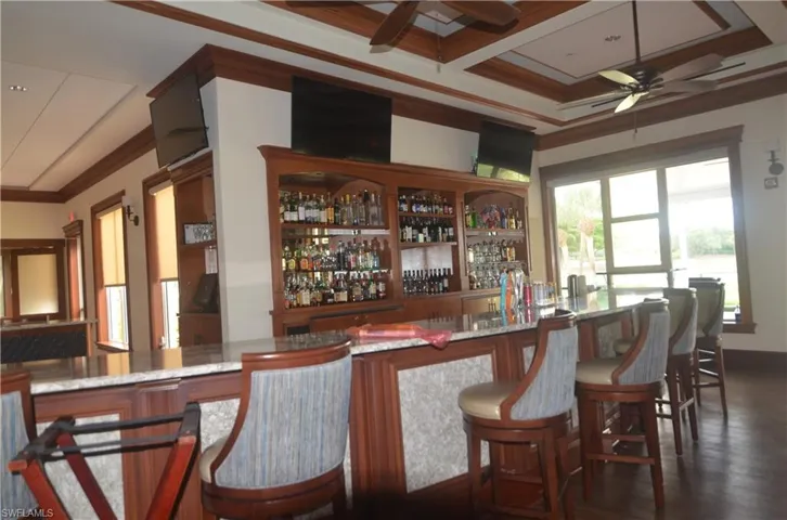 Indoor wet bar with ceiling fan, crown molding, coffered ceiling, beamed ceiling, and dark wood-type flooring