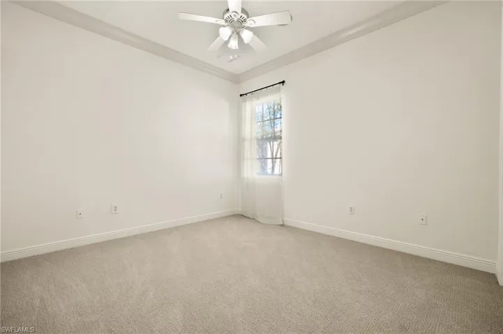 Spare room featuring light colored carpet, crown molding, baseboards, and ceiling fan