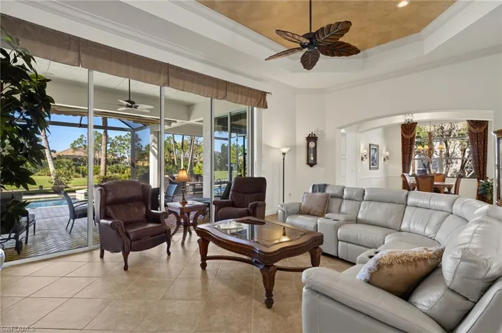 Living room with arched walkways, light tile patterned floors, ornamental molding, a ceiling fan, and plenty of natural light