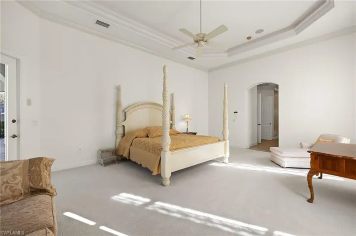Bedroom with carpet, a tray ceiling, arched walkways, and crown molding