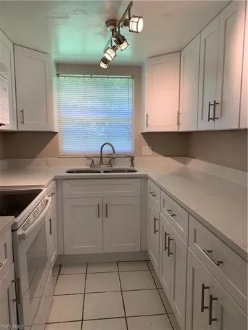 Kitchen with white cabinets, light tile patterned floors, light stone countertops, range, and sink