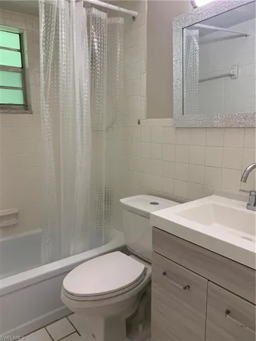 Full bathroom with toilet, tile patterned floors, shower / bath combo with shower curtain, tile walls, and vanity