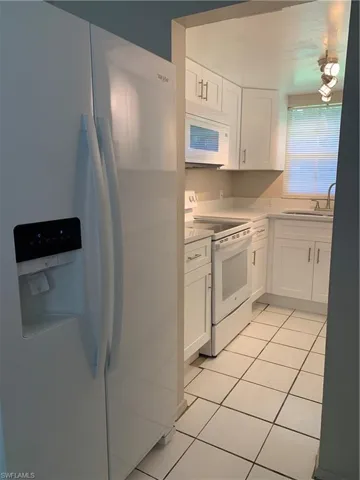 Kitchen featuring white cabinetry, white appliances, and light tile patterned flooring