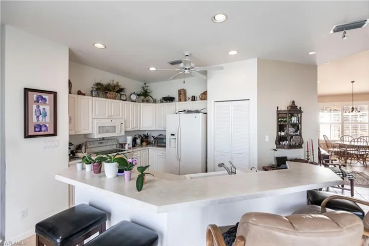 Kitchen featuring white appliances, ceiling fan, a kitchen breakfast bar, and white cabinetry