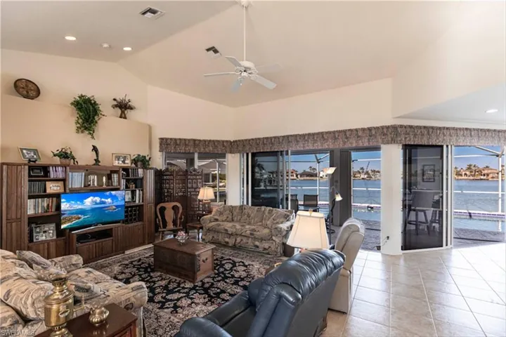 Living room featuring light tile patterned floors, ceiling fan, vaulted ceiling, and a water view